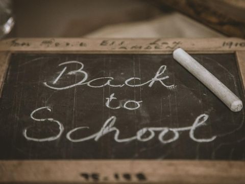 Kleine Tafel mit der Aufschrift ‚Back to School‘ in Kreide, daneben ein Stück Kreide
