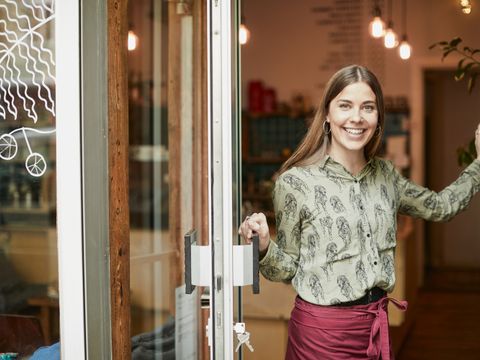 Coffee shop owner holding the door open and looking at camera. Portrait with copy space.