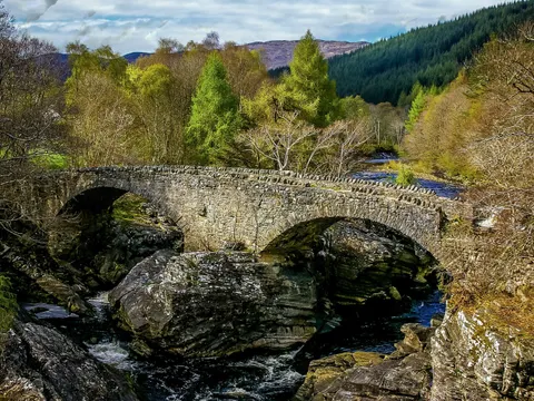 Historische Exkursionen und Vorträge, alte Steinbrücke mit zwei Bögen, die über einen FLuss führt. An dne Ufern sind Felsen und Bäume zu erkennen.