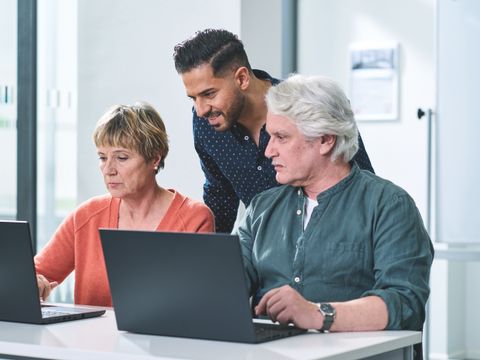 Drei Teilnehmende vergleichen Arbeitsergebnisse an zwei Notebook-Bildschirmen.