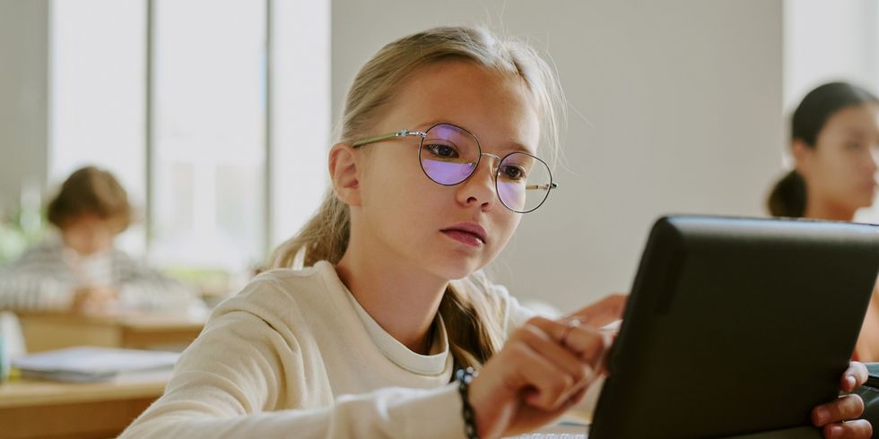 Schülerin sitzt im Klassenzimmer und benutzt ein Tablet