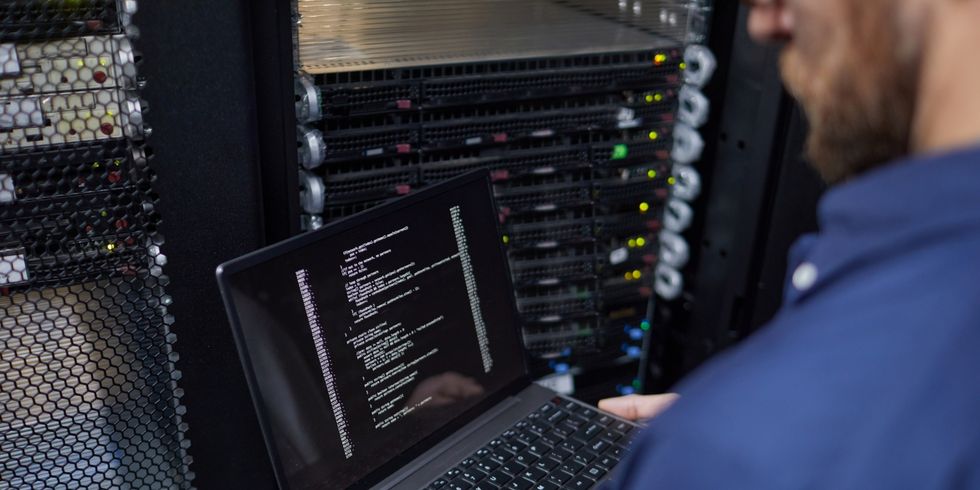 Techniker steht im Serverraum mit Laptop in der Hand.
