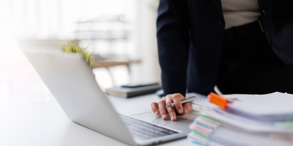 Frau arbeitet an einem Laptop und Papierstapel