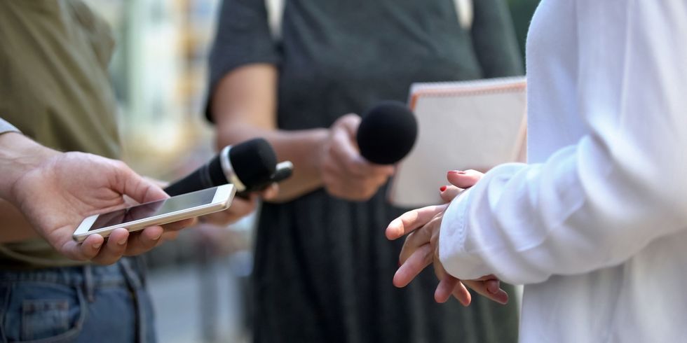Zwei Personen mit Mikrofonen und Smartphones, die eine dritte Person interviewen
