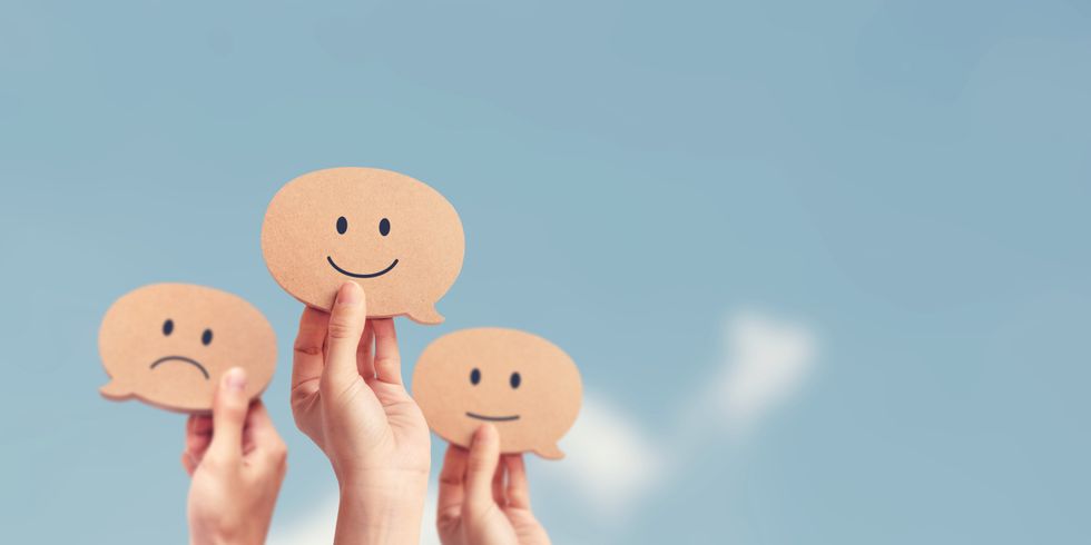 Hände zeigen Bewertungen mit Smileys vor Himmelshintergrund