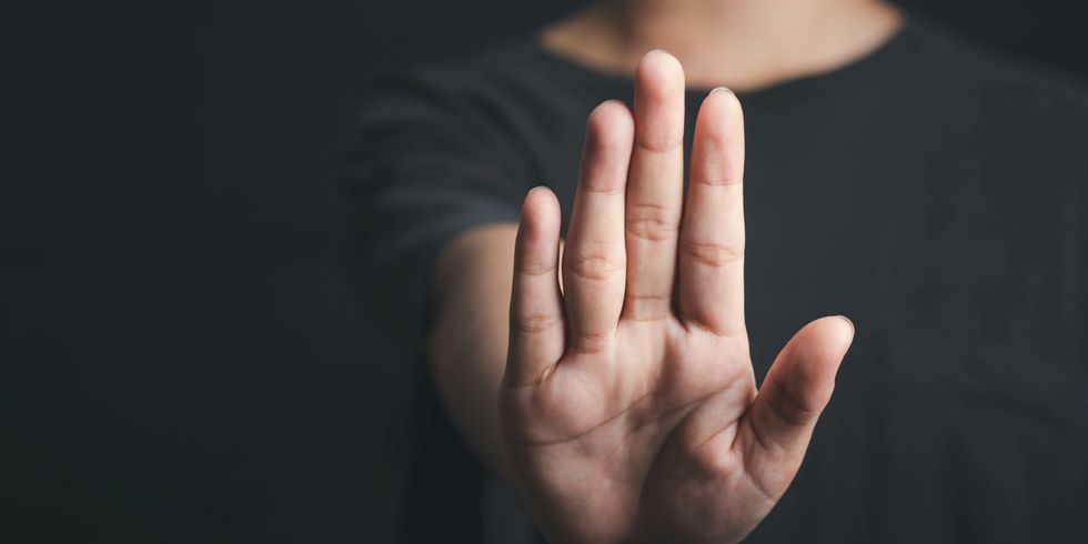Nahaufnahme einer Hand, die nach vorne gehalten wird, als Signal für ‚Stopp‘ oder ‚Halt‘, vor unscharfem Hintergrund.