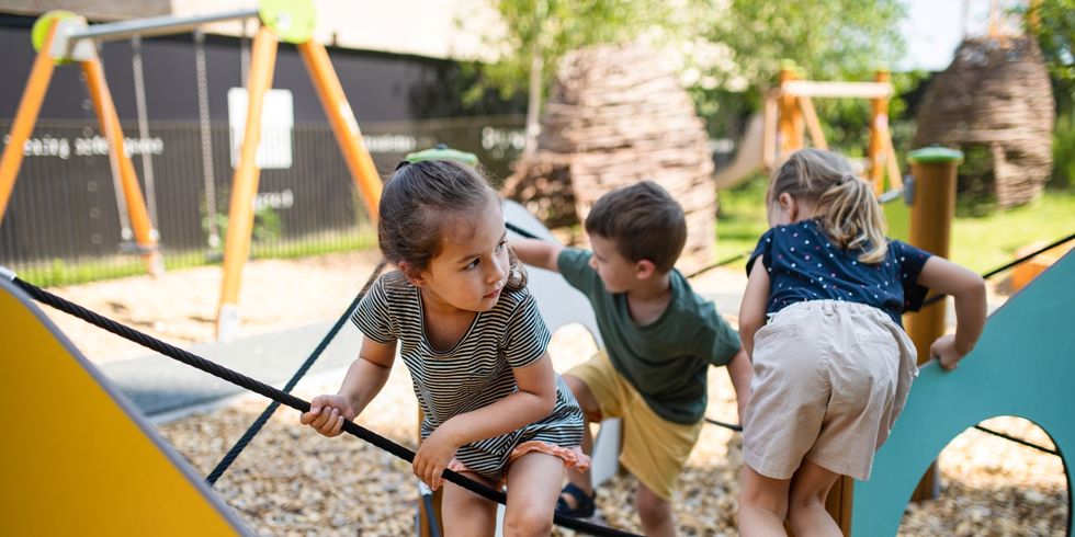 Drei Kinder spielen auf einem Klettergerüst im Freien mit Holzschnitzelboden