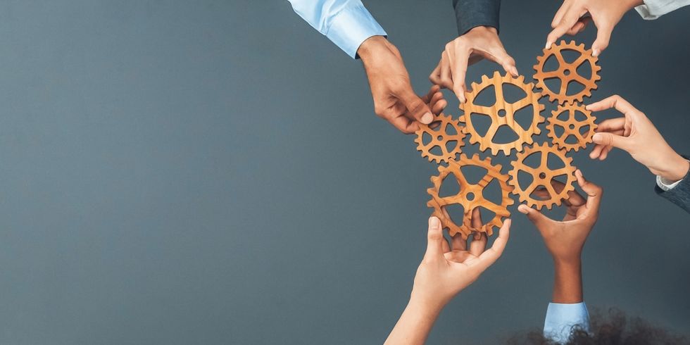 Mehrere Hände greifen nach ineinandergreifenden Zahnrädern aus Holz, symbolisieren Zusammenarbeit, Teamwork und das Zusammenspiel von Prozessen.