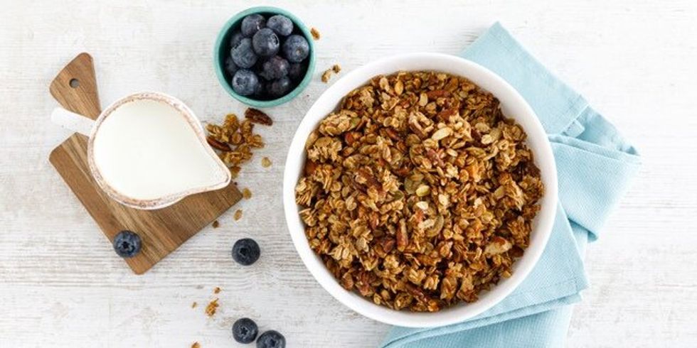 Müsli steht auf einem hellblauen Tuch mit einem Kännchen Milch und Heidelbeeren