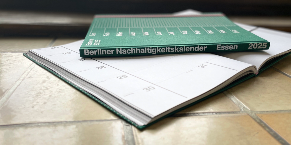 Zwei Exemplare des Berliner Nachhaltigkeitskalender 2025, ein aufgeschlagenes mit Wochenansicht 25. bis 30. August, ein geschlossenedes in dunkelgrün mit entsprechender Aufschrift "Berliner Nachhaltigkeitskalender "Essen" 2025"