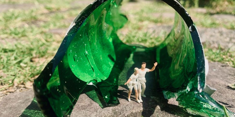 Großaufnahme aus der Ausstellung "So klein! So groß" im Schoeler Schlösschen: eine zerbrochenede grüne Glasfalsche, in den Scherben zwei Miniaturfiguren, die Arm in Arm herauslaufen