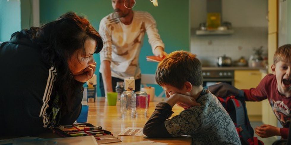 Standfoto aus dem Dokumentarfilm "Im Prinzip Familie". Eine Erzieherin hilft einem Jungen bei den Hausaufgaben.