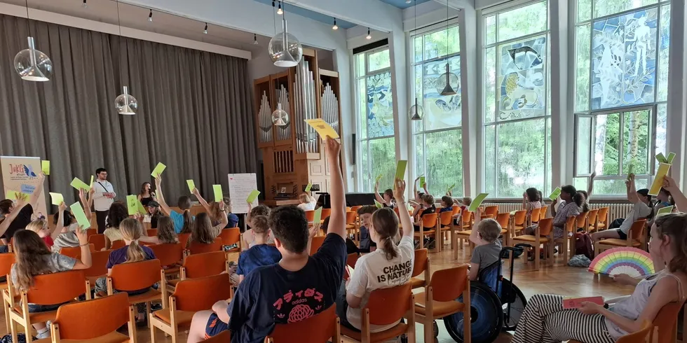 Kinder und Jugendliche sitzen in großem Saal