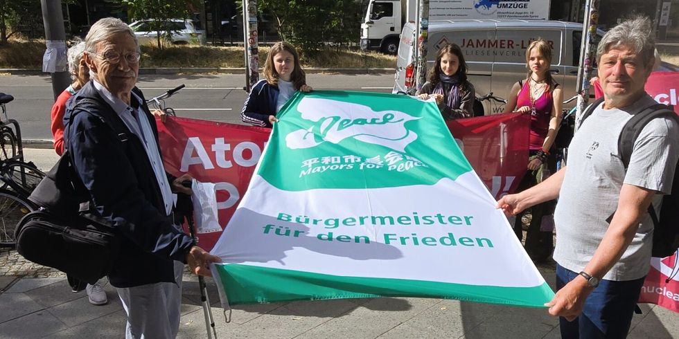 Clara Herrmann zeigt gemeinsam mit Aktivist*innen die Flagge der "Mayors for Peace" vor dem Rathaus in Friedrichshain