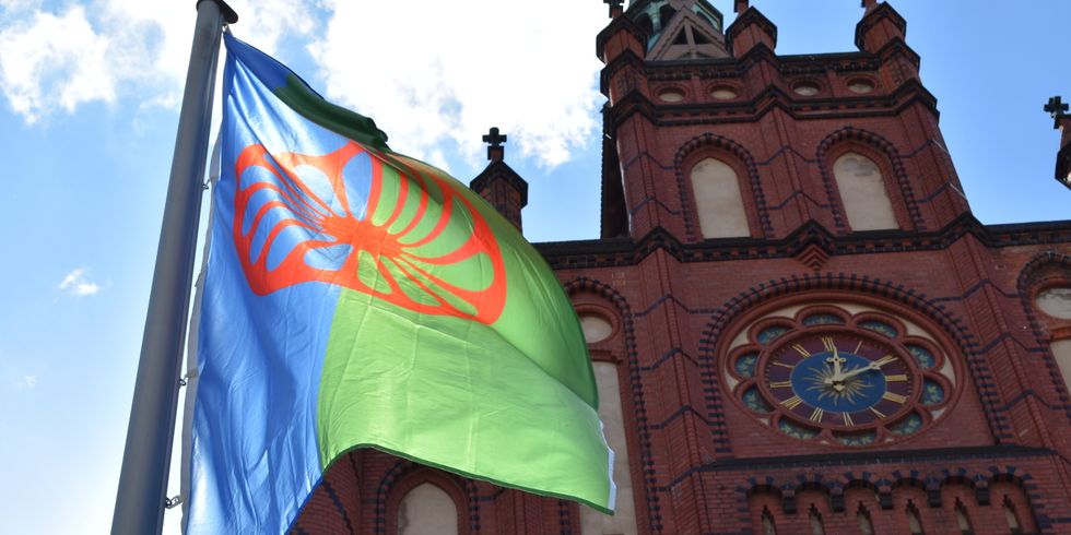 Blau-grüne Romaflagge mit rotem Rad vor dem Lichtenberger Rathaus