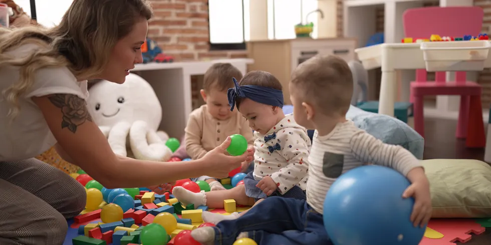 Bild - Kinder sitzen auf dem Boden und spielen mit der Erzieherin