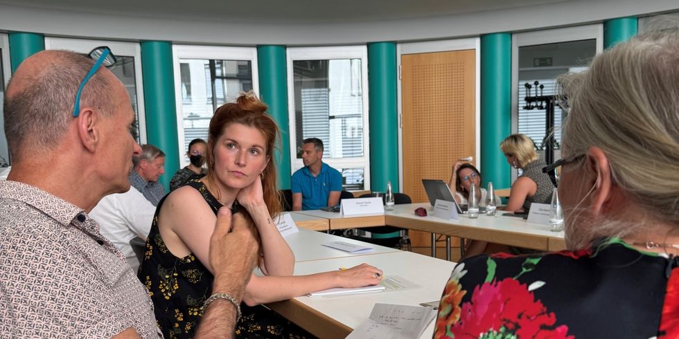 Teilnehmende des Klimarats sitzen an einer Tafel aus Tischen und unterhalten sich in Kleingruppen