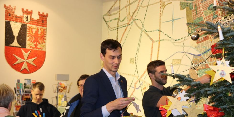 Bezirksbürgermeister Hikel schmückt den Wunschbaum im Foyer des Rathause mit den Wunschsternen der Kinder.