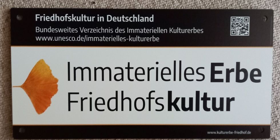 Eine Tafel an einer Wand mit der Aufschrift "Immaterielles Erbe Friedhofskultur"