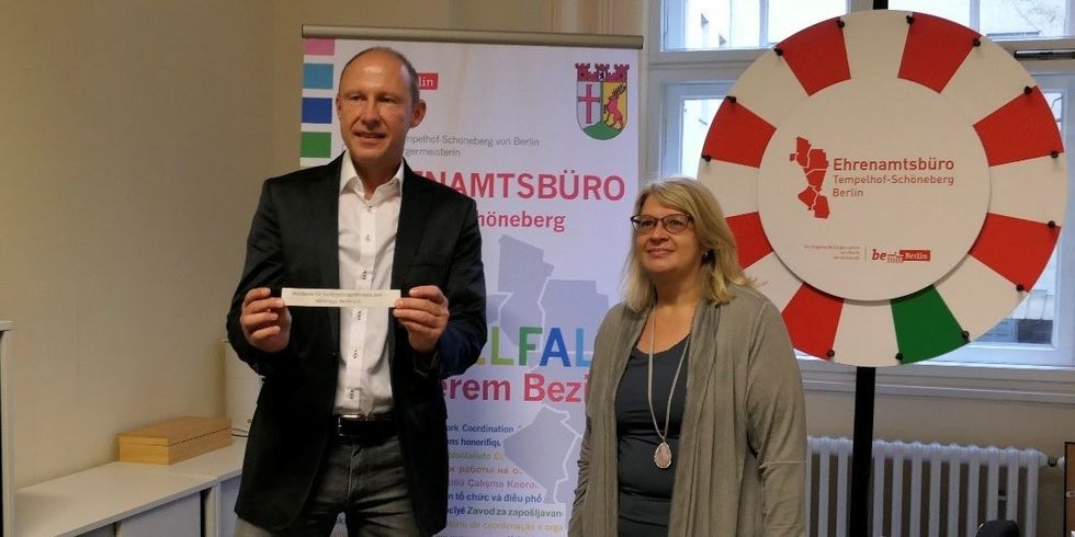Eine Frau und ein Mann halten einen Zettel in die Kamera und freuen sich.