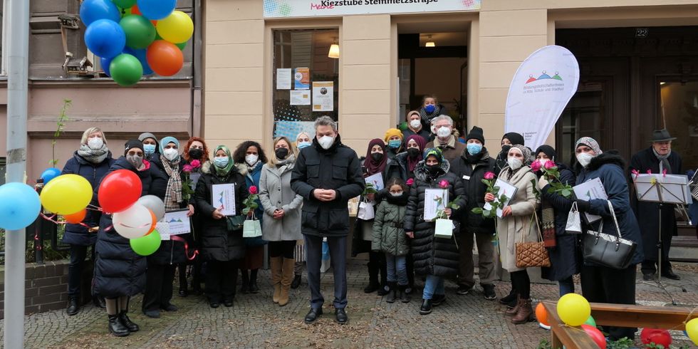 Ein Mann steht mittig in einer Gruppe von Personen mit Urkunden. Rundherum sind Luftballons verteilt.