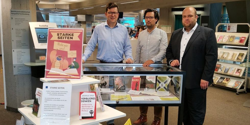 Drei Männer stehen hinter einer Glasvitrine mit Büchern. Vor der Vitrine ist ein Tisch mit den gleichen Büchern und einem Aufsteller unter der Überschrift "Starke Seiten".