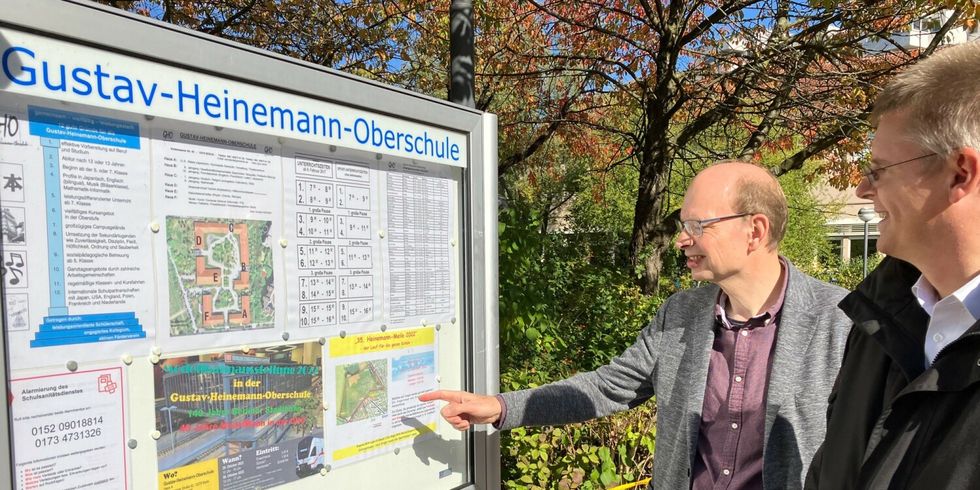 Zwei Männer schauen eine Informationstafel der Gustav-Heinemann-Oberschule an.