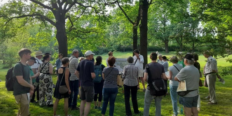Eine Gruppe von Menschen steht in einem Park und schaut zu zwei Personen, die zusammen eine Karte hochhalten.