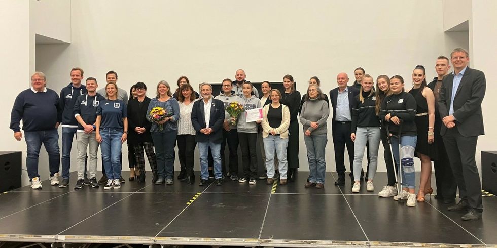 Viele Menschen stehen auf einer Bühne nebeneinander und blicken gücklich in die Kamera.