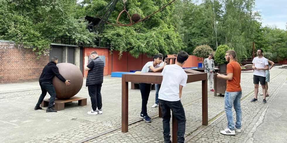 Jugendliche betrachten Metallskulpturen, darunter auch eine große Kugel.
