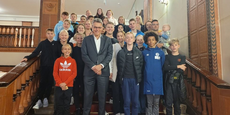Eine Gruppe von Menschen, hauptsächlich Kinder, steht auf einer Treppe in einer Halle. Im Vordergrund steht ein Mann und lächelt in die Kamera.
