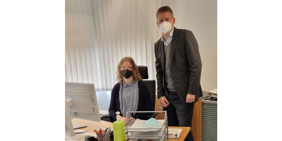 Junge Frau sitzt am Schreibtisch und neben ihr steht ein Mann