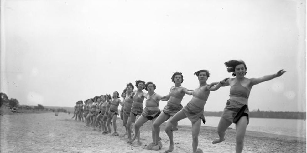 Frauen tanzen in einer langen Reihe am Strand.