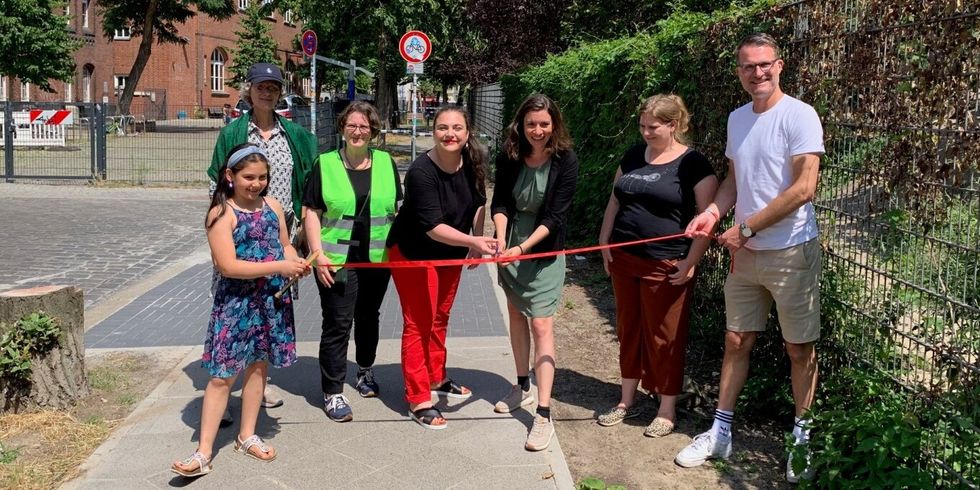 Sieben Personen zerschneiden ein rotes Band auf einem Gehweg