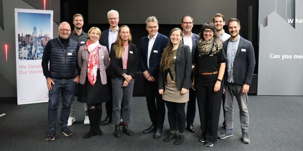 Eine Gruppe Menschen steht zusammen in einem Saal und lächelt in die Kamera.