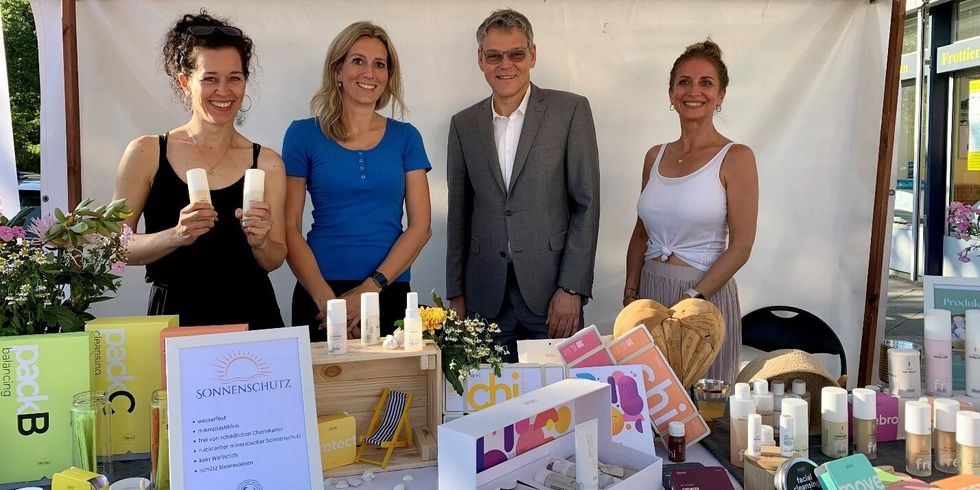 Drei Frauen und einen Mann stehen an einem Stand mit Kosmetikprodukten