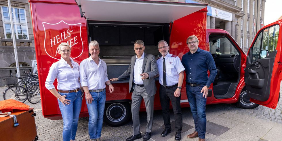 Fünf Personen stehen vor einem roten Kleintransporter mit mobiler Küche und Ausgabe.