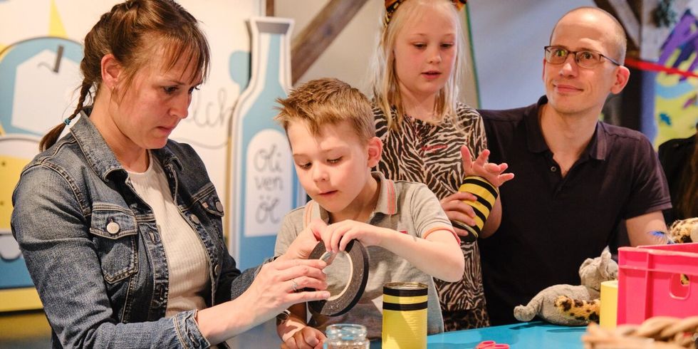 Eine Frau, ein Mann und zwei Kinder sitzen zusammen an einem Tisch mit Bastelmaterialien und basteln etwas.