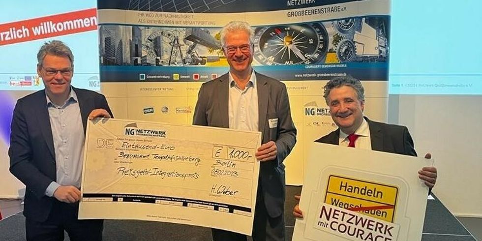 Drei Männer stehen mit einem großen Scheck über 1.000 Euro und einem Plakat mit der Aufschrift "Handeln Netzwerk mit Courage" vor der Kamera.