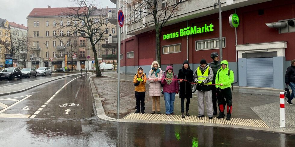 Sieben Personen stehen an einem Kreuzungsbereich und zerschneiden ein rotes Band.