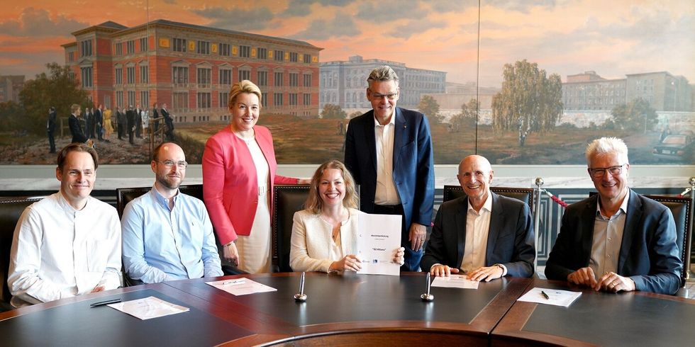 Fünf Personen sitzen an einem Tisch un zwei stehen hinter ihnen