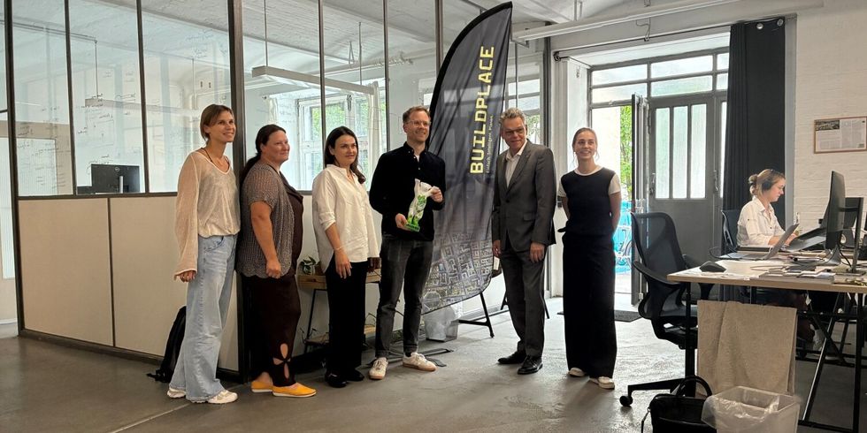 Sechs Personen stehen nebeneinander. Hinter ihnen steht eine Beachflag, auf der Buildplace steht.
