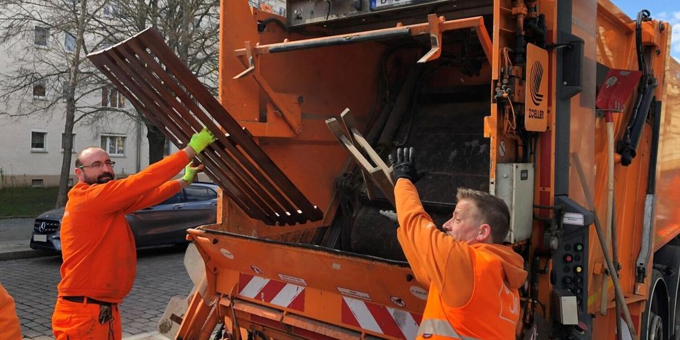 Zwei Männer in Arbeitskleidung heben Sperrmüll in die Schüttung eines Müllfahrzeugs.