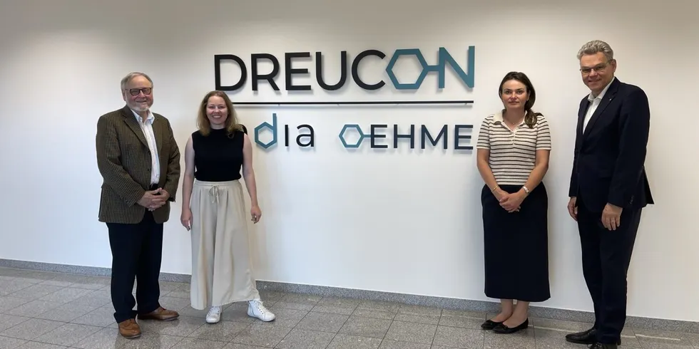 Vier Personen stehen vor einer Wand, auf der DREUCON, India, OEHME steht.