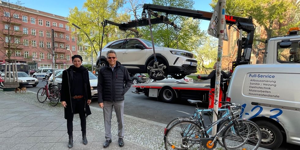 Zwei Personen stehen vor einem Wagen, der gerade abgeschleppt wird.