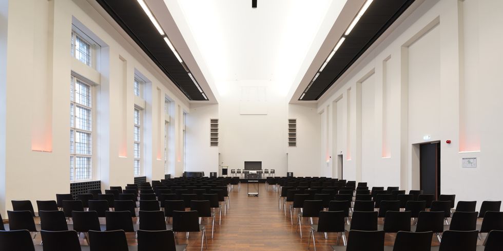 großer länglicher Saal mit Stühlen, die richtung Bühne gerichtet sind