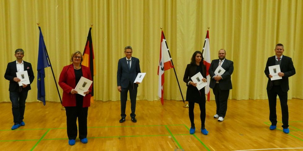 2 Frauen und 4 Männer stehen vor Fahnen