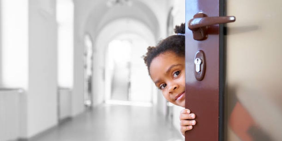 Pretty African girl hiding from opened door in school.