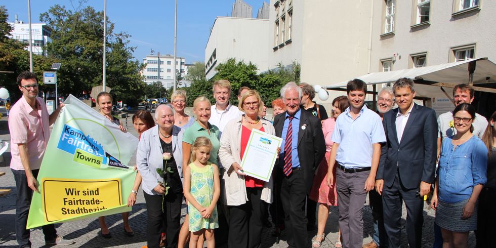 Zu sehen ist ein Gruppenbild aller Fairtrade Aktiven im Bezirk. Sie halten eine Fahne mit der Aufschrift "Wir sind Fairtrade Stadtbezirk" hoch