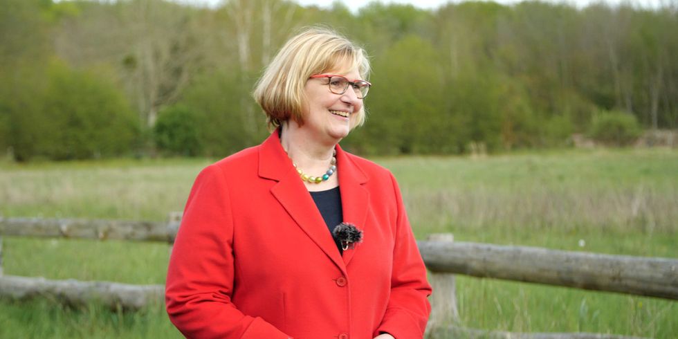 Eine Frau in roter Jacke steht vor grüner Wiese